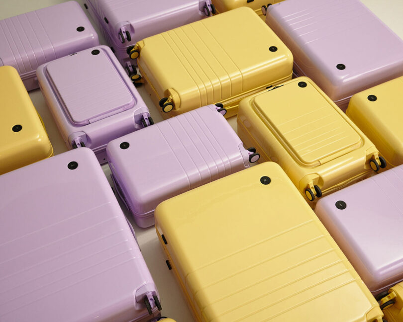 Monos and Magnolia Bakery collaboration of hard case luggage finished in banana yellow and purple icing color finishes arranged on the floor in a loose grid.