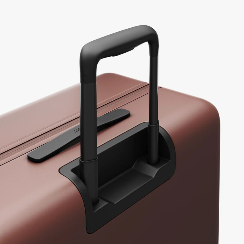 Close up detail of a Terracotta colored Monos Check-In hard case luggage's telescoping black handle