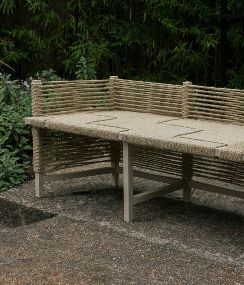A wooden bench has a woven cord seat and cord back