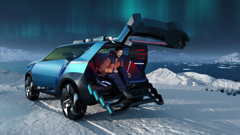 Man in warm outdoor puffy jacket and snow gear seated in the back of the sharply paneled icy blue Nissan Hyper Adventure concept render set in a snowy setting with the Northern Lights glowing in the background with an Arctic body of water just a few feet away. The back of the vehicle has a set of four retractable steps leaning outward up to a bucket-style sofa seat where the man is seated.