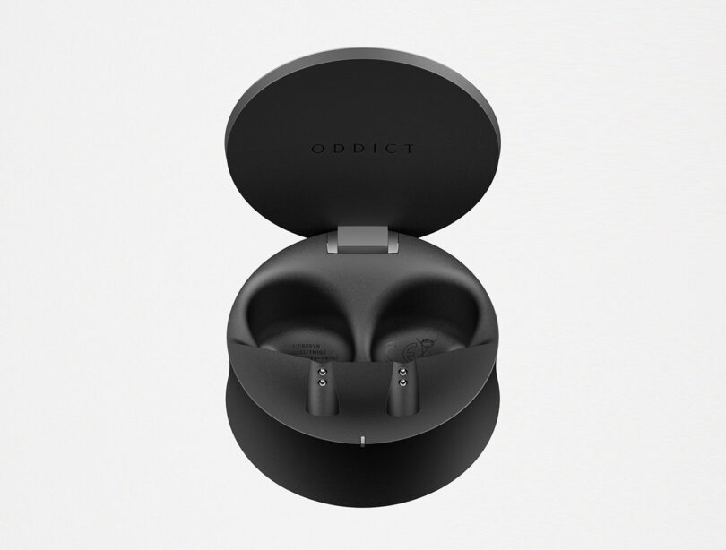 Open case of the TWIG 2 wireless earbuds revealing the two indented slots where each earbud recharges. Interior is all black molded plastic, with subtle "ODDICT" branding on the underside of the case.