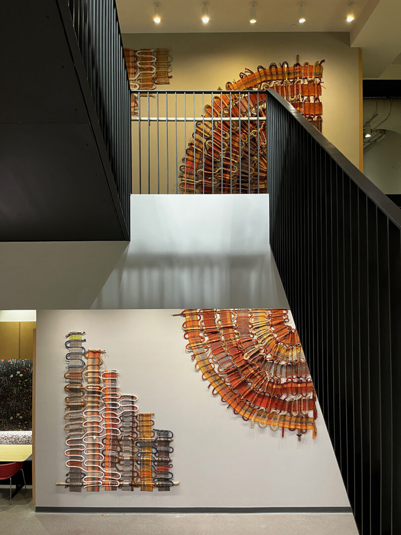 two floors displaying large handwoven art pieces with a staircase connecting them