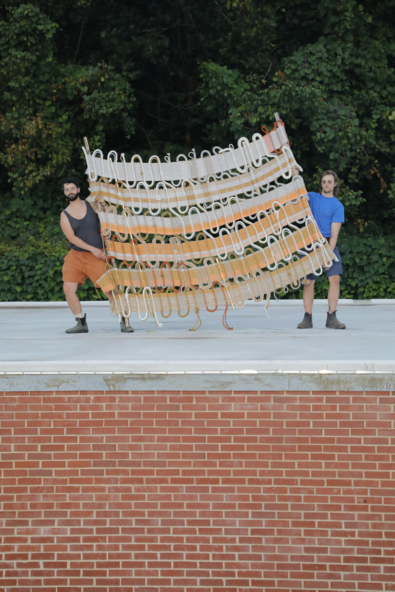 two people hold up a large section of a handwoven artwork