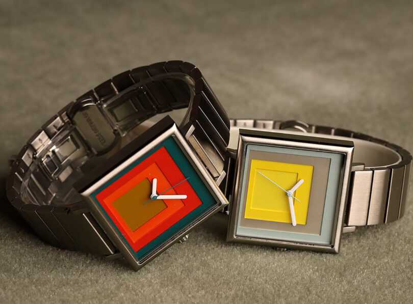 Close up of both Josef Albers inspired Project Watches, featuring laser cut squares of color inside a 35mm stainless steel square shaped watch case with stainless steel band, staged across a soft carpet surface.