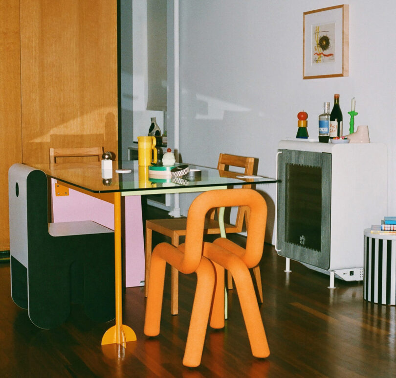 The Super Smart Fridge drinks fridge set in a small dining environment surrounded by contemporary curvy seating, glass dining table, with a selection of cocktail drink bottles set on top of the refrigerator.