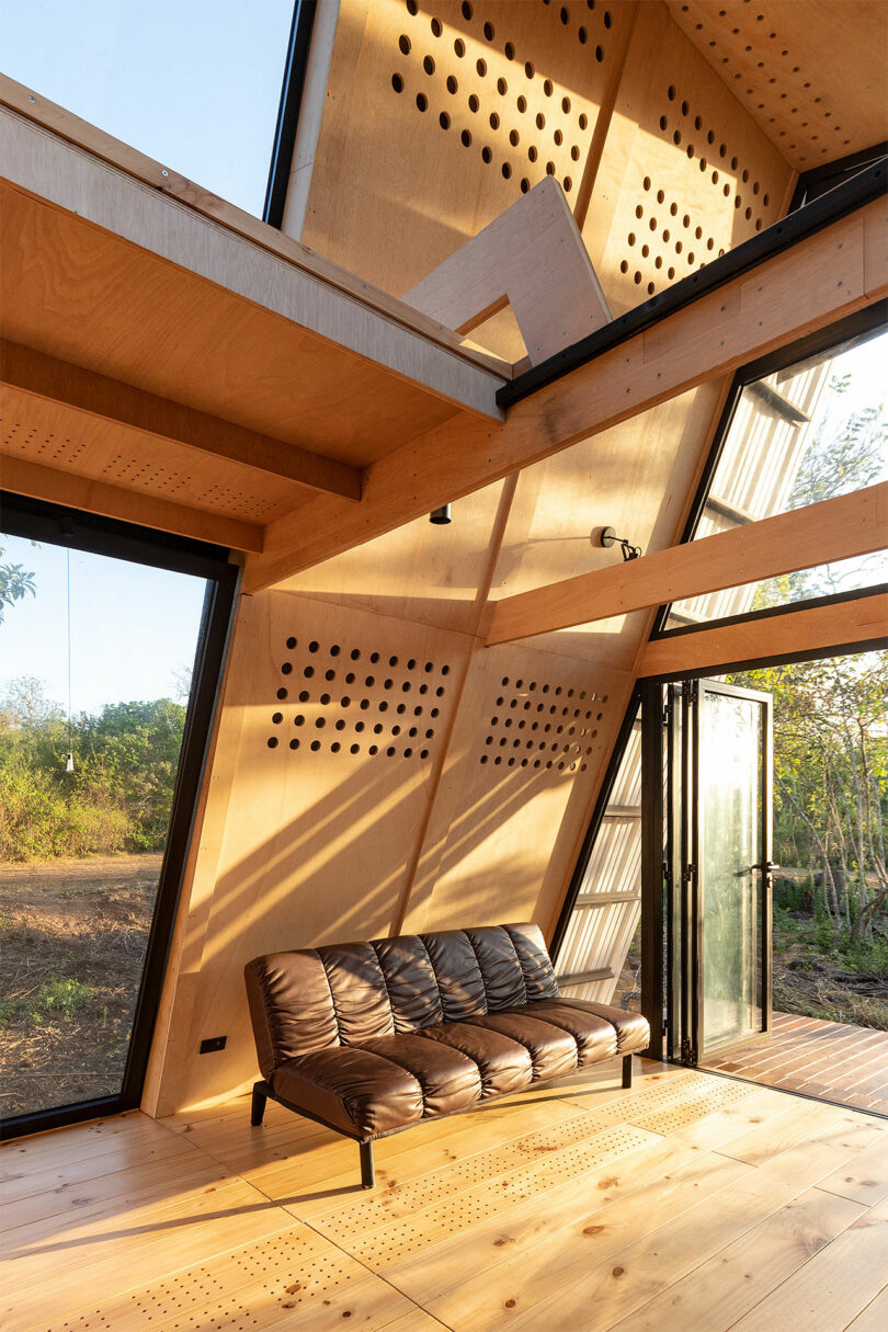 vista interna em ângulo da cabine com estrutura em A, paredes de madeira inclinadas e pequeno sofá marrom