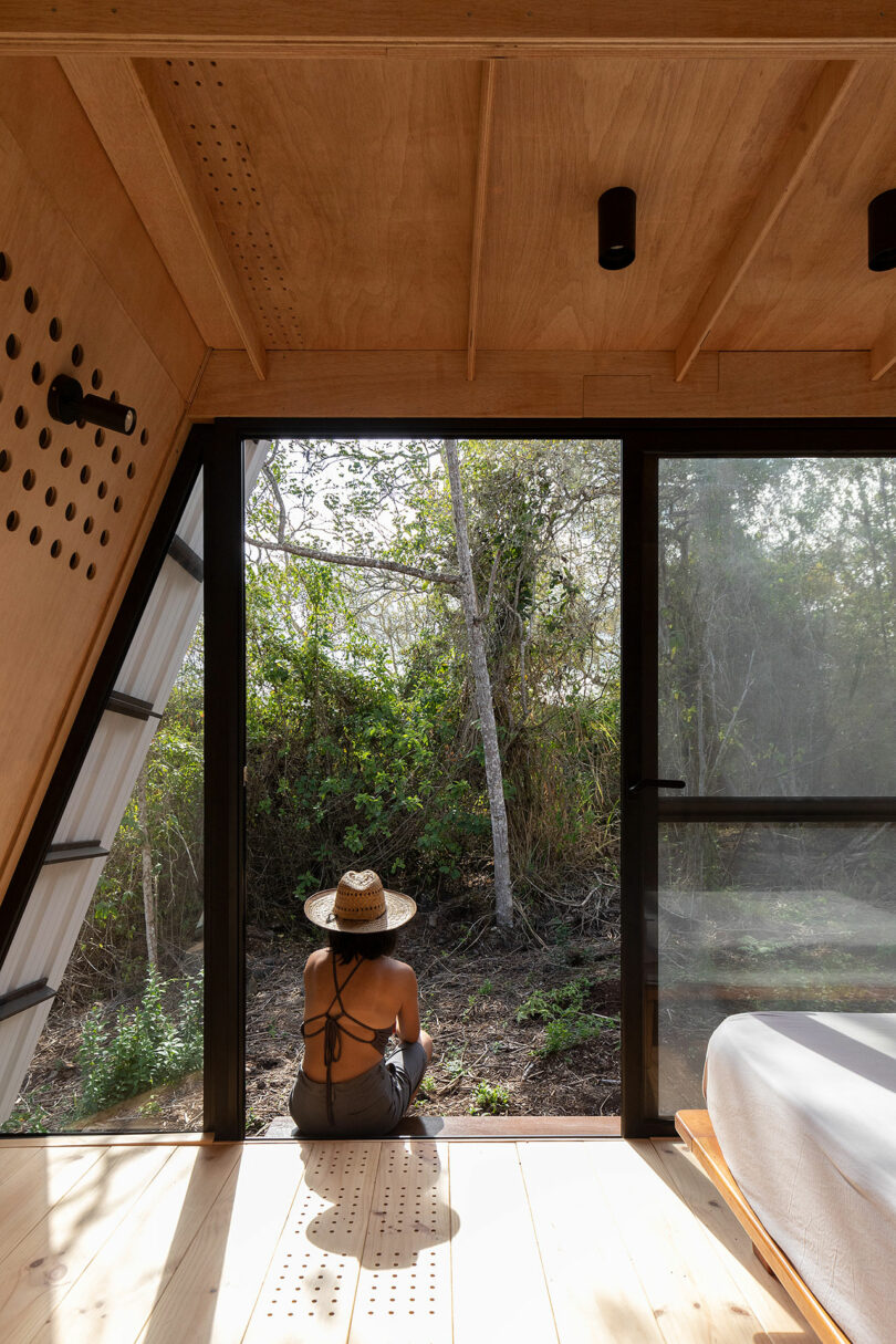 vista parcial do interior de uma cabana minimalista com uma mulher sentada em uma varanda do lado de fora