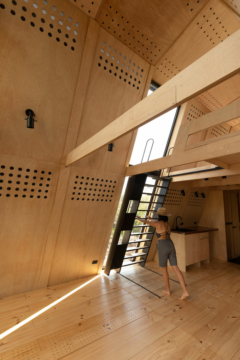 vista interna em ângulo da cabine com estrutura em A, paredes de madeira inclinadas e escada móvel