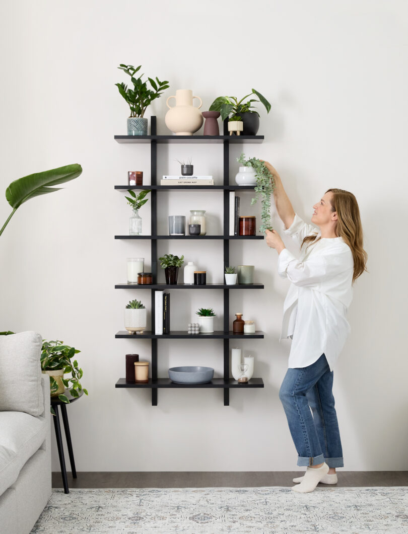 woman styling modular black shelf holding various plants, books, and objects