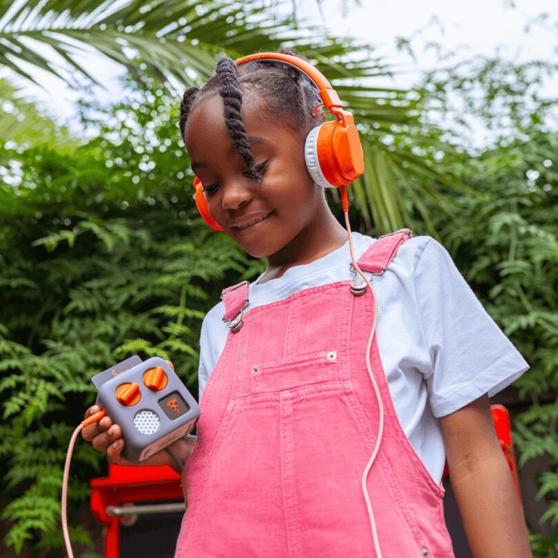 African American girl wearing pink overalls listening to a player with headphones