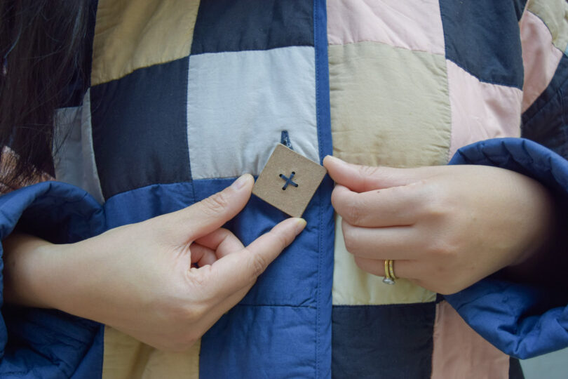 two hands touching a ceramic button on a quilted coat