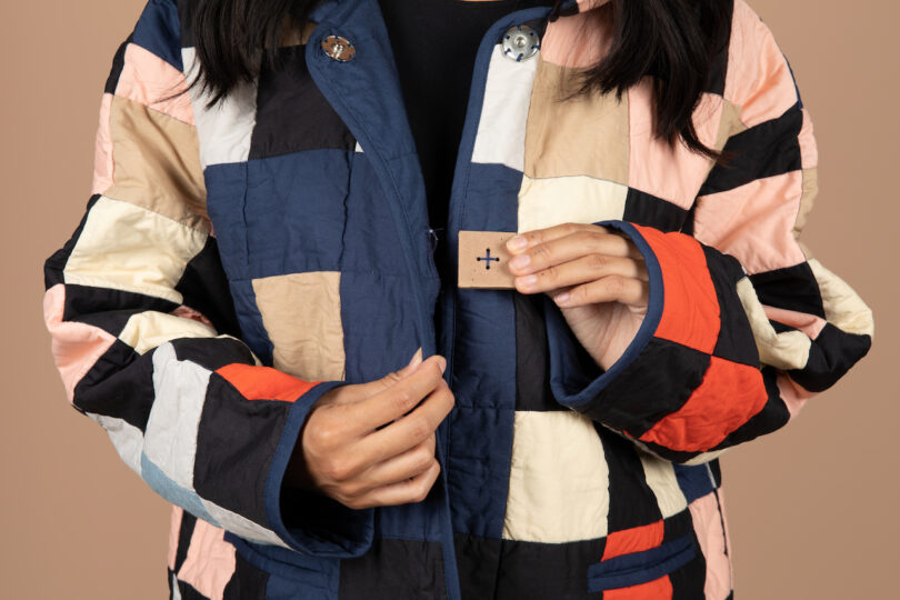 woman wearing a patchwork quilted coat with her hand holding onto the ceramic button