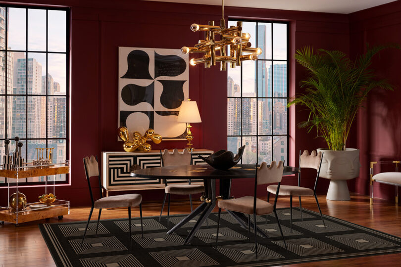 Glamorous living room done in sumptuous red walls and modern Jonathan Adler styled decor with large black area rug in the middle.