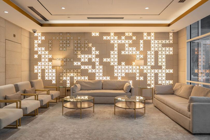 styled indoor commercial seating area with neutral chairs and sofas, two round coffee tables, and a feature wall using square blocks of lighting