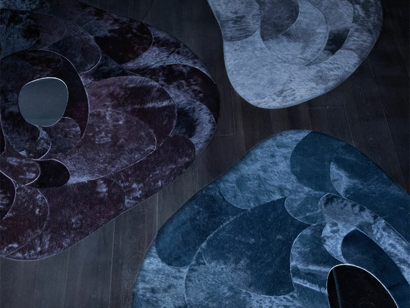 Three amorphous hide rugs in inky hues with mirrors in the center.