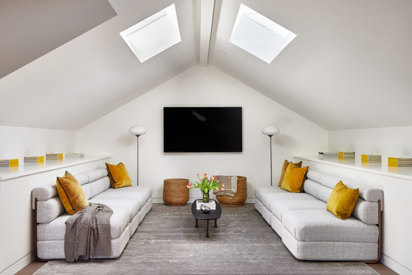 white styled interior space with large skylights, two white sofas, and wall-mounted television