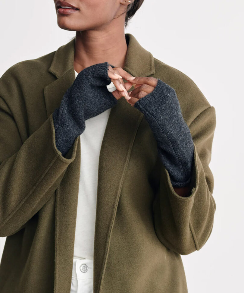light-skinned woman wearing a olive colored coat and dark grey fingerless gloves