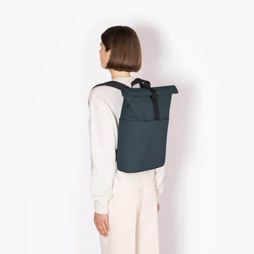 light-skinned person with their back to the camera models a dark green modern backpack