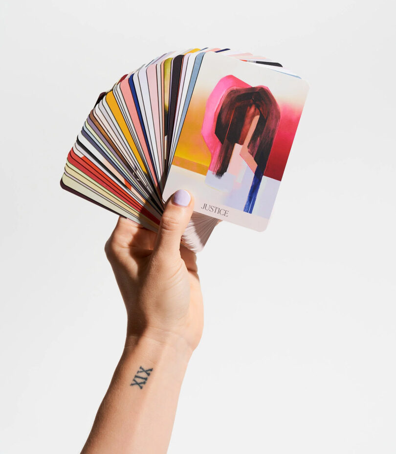 light-skinned hand holding a deck of oracle cards up against a white background