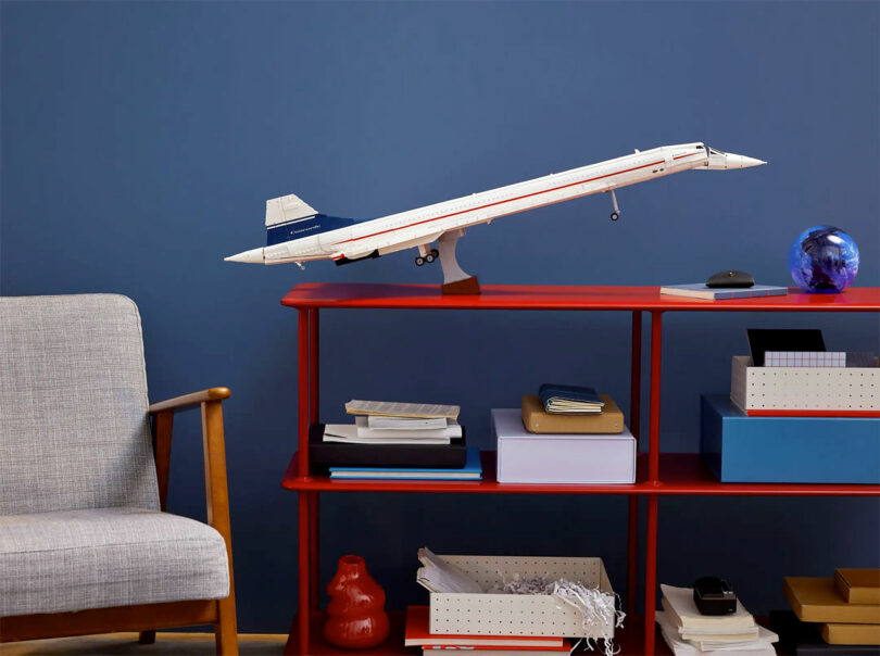 built Concorde LEGO model on red shelf in front of deep blue wall