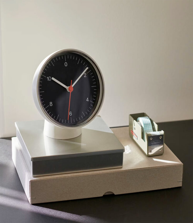 styled shot of white circular desk clock with black face on top of 2 boxes