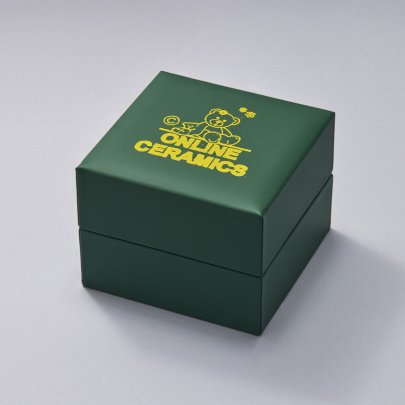 Green closed box of the Online Ceramics x Hodinkee Casio G-SHOCK digital watch with Online Ceramics logo in yellow with teddy bear graphic