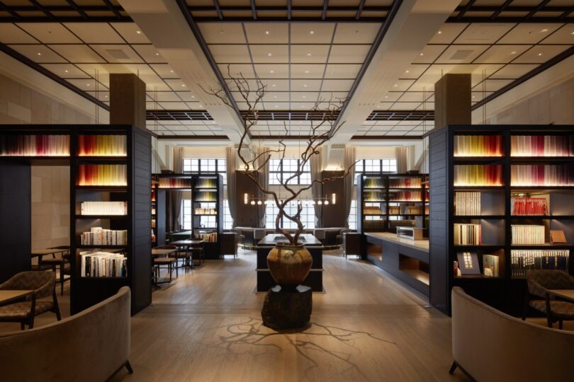 The Hotel Seiryu Kyoto Kiyomizu's library themed restaurant with large bookshelves a large tree in a large pot centerpiece illuminated from overhead.