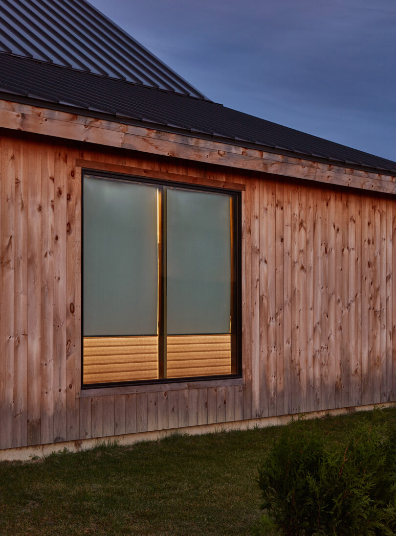 Exterior of wood clad home's windows with the shades partially drawn down and integrated LED lights on.