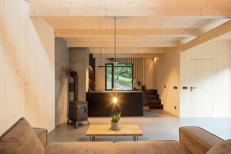 view into modern black kitchen with light wood ceiling and simple staircase behind