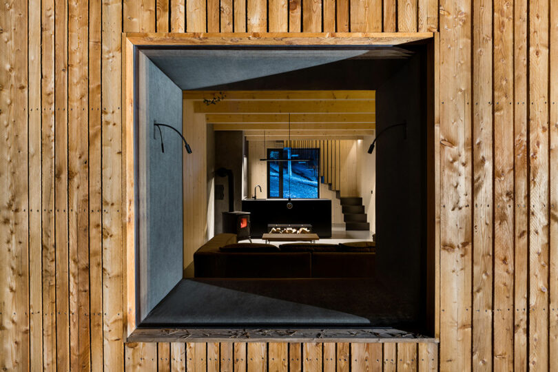 closeup view of modern wood cabin's exterior looking through black square window into interior