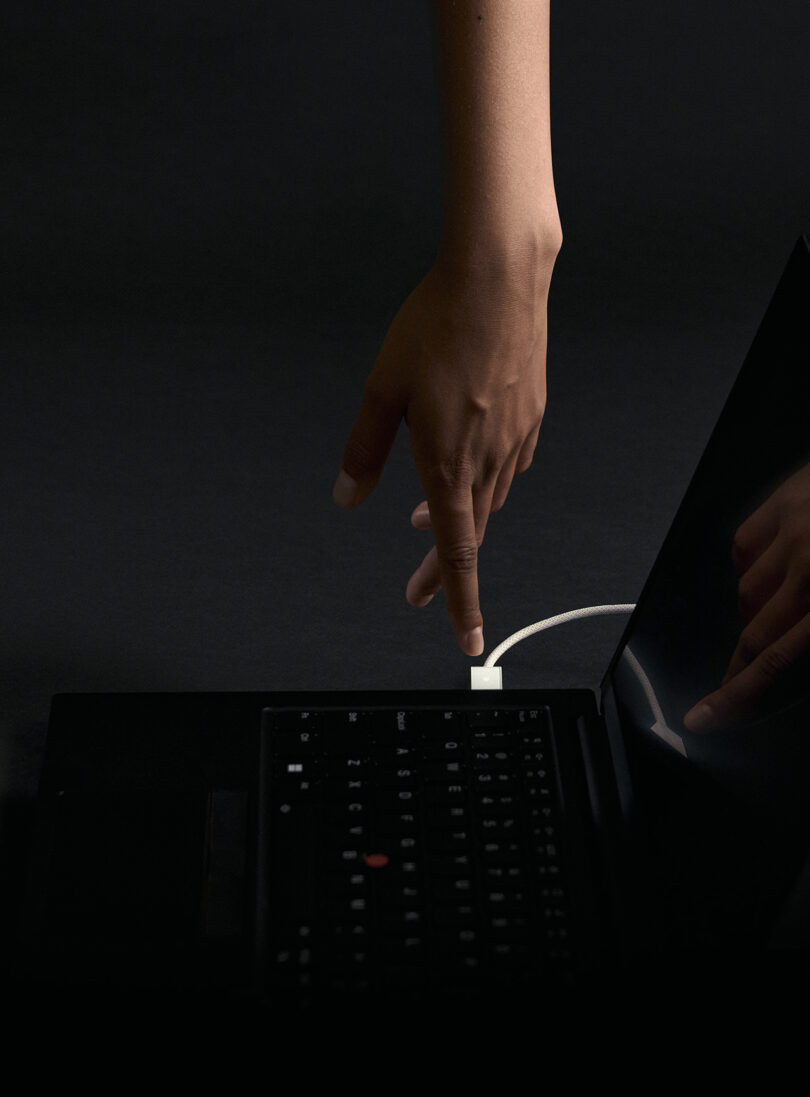 Person's hand pointing toward Opal Tadpole webcam connected to laptop USB port