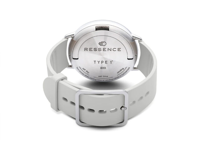 Back view of the Ressence TYPE 1° Round M wristwatch with light gray wristband and a casebook winding mechanism. Back plate is inscribed with "RESSENCE TYPE 1 033"