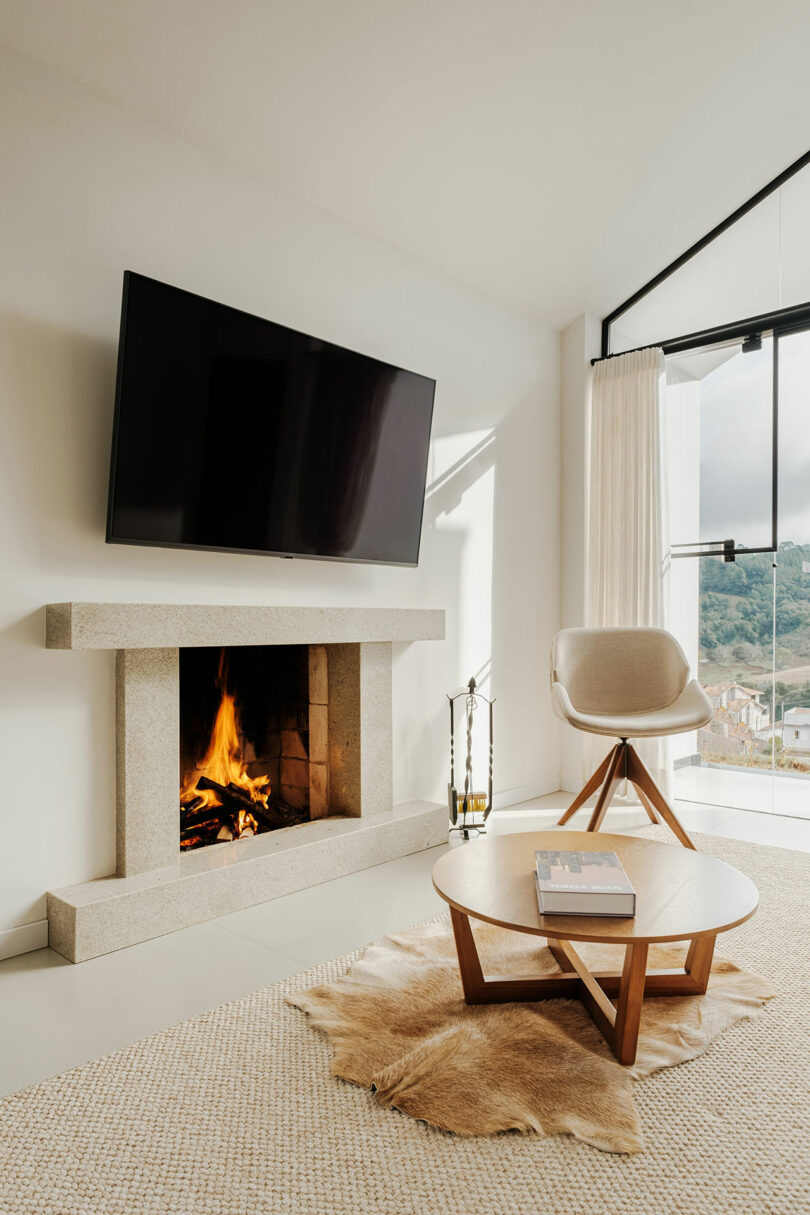 angled interior view of modern white living room with TV over burning fireplace