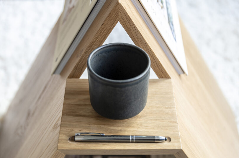 detalhe de mesa lateral de madeira em formato de triângulo segurando um livro e uma caneca