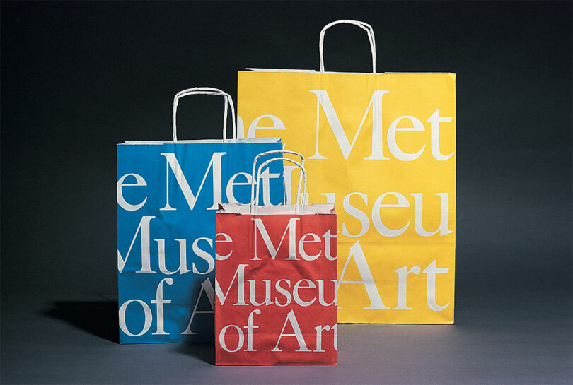 Three shopping bags in yellow, red, and blue with white print featuring the Metropolitan Museum of Art