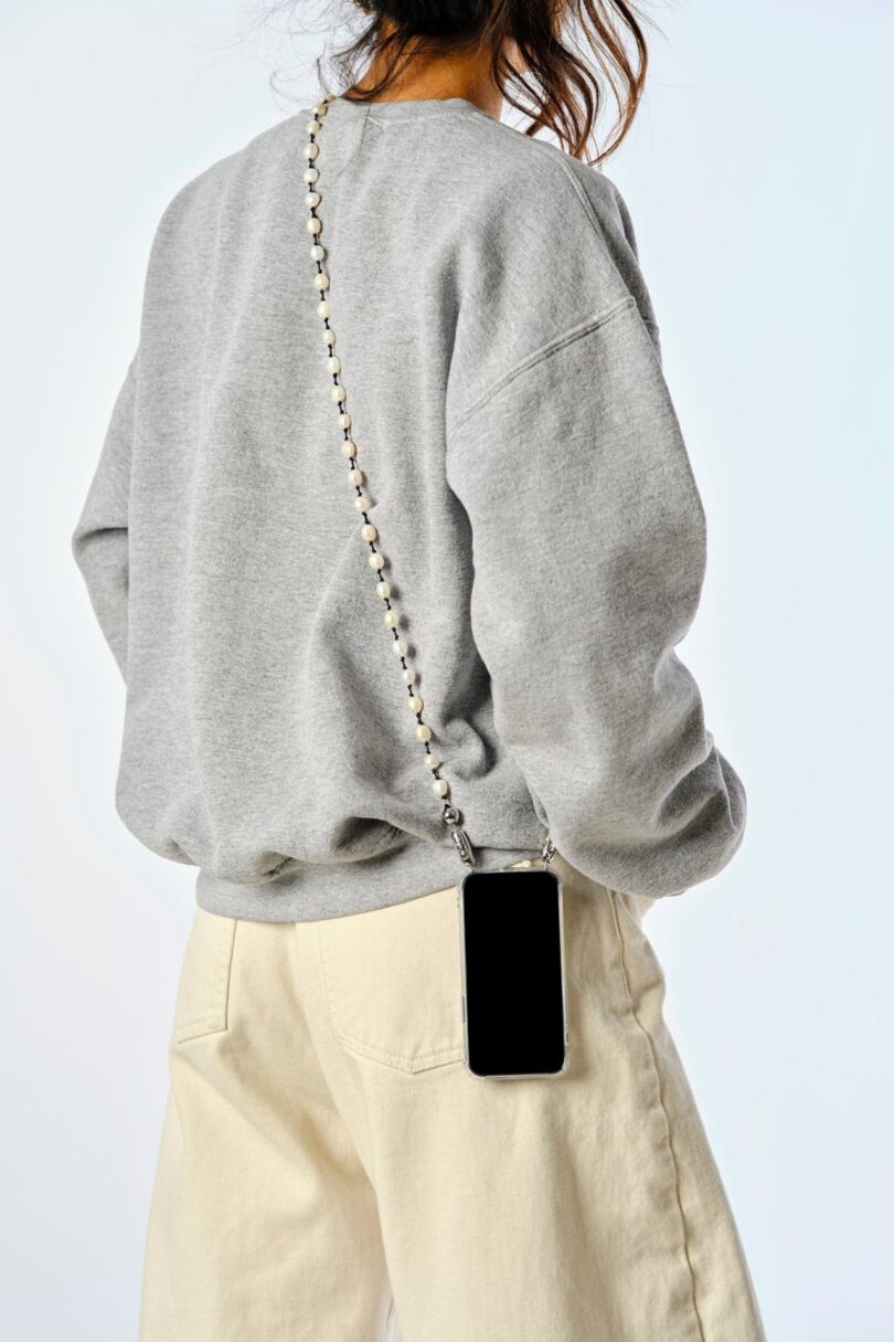 woman in grey sweatshirt wearing a pearl crossbody phone chain
