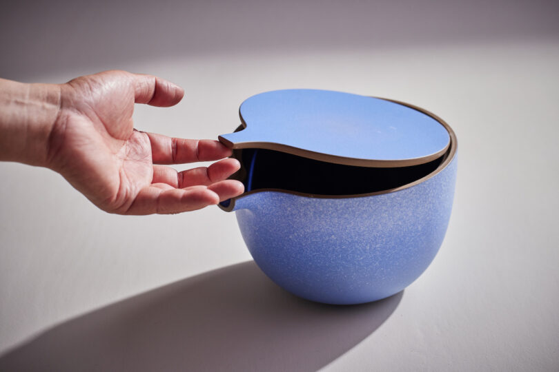 hands lifting top off blue ceramic bowl with spout