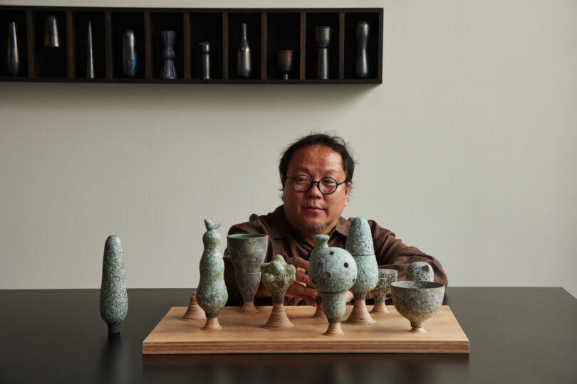 man behind a wooden tray of ten ceramic objects