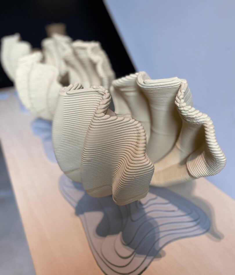 Three large clam-shell forms stand open, the layers of 3D-printed filament clearly visible. 