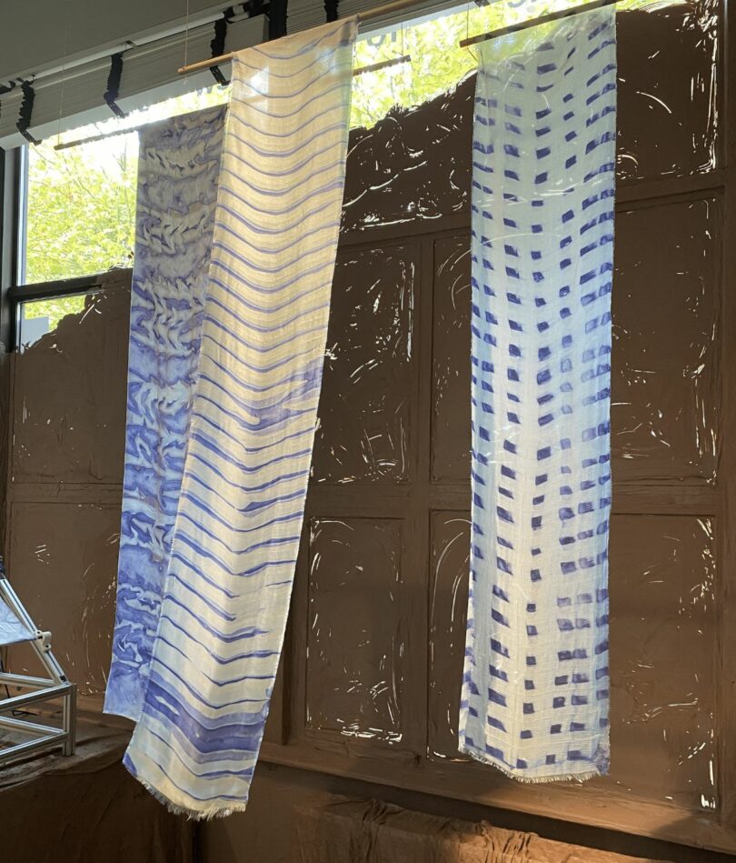 Three pieces of blue and white fabric hand from horizontal bamboo poles and sway in the breeze. 