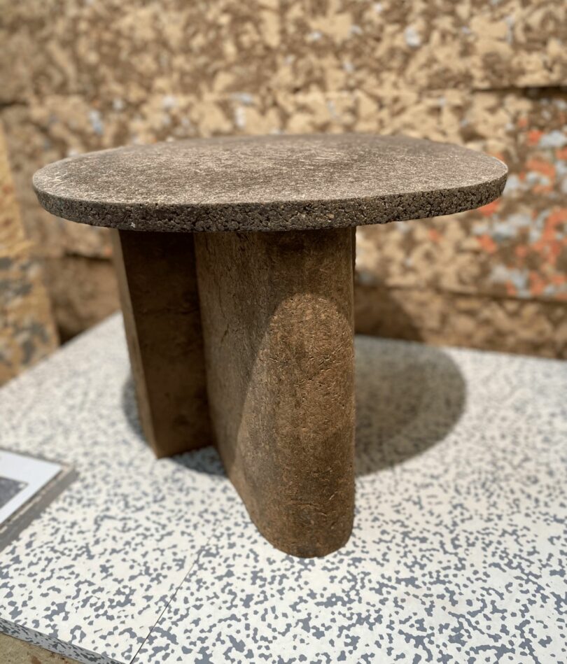 A small round side table with a rounded leg is made from a brown fibrous material