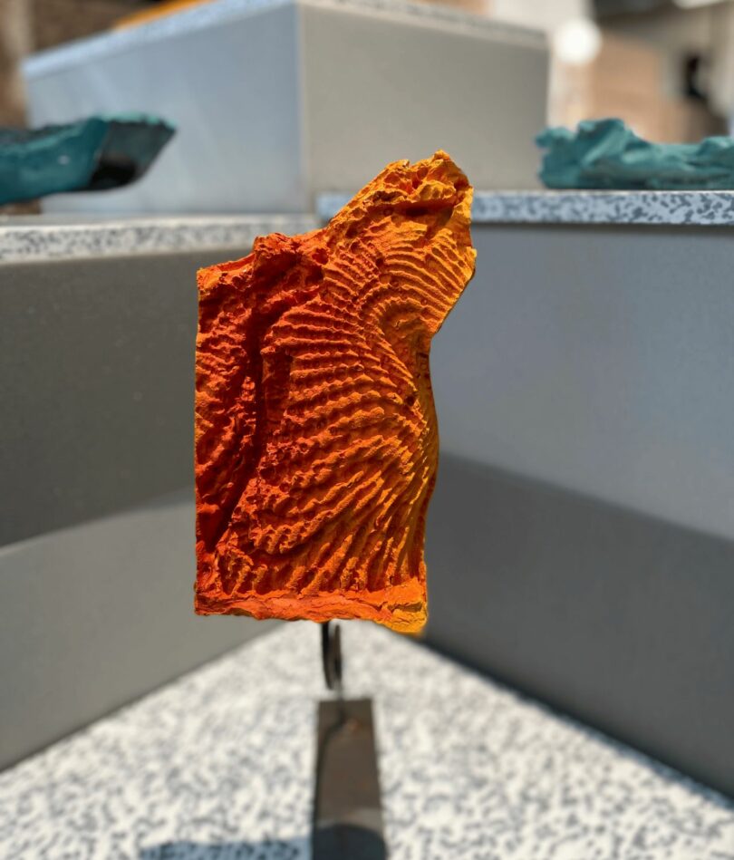A bright orange piece of material is on a stand – it has rippled in the surface like sound waves