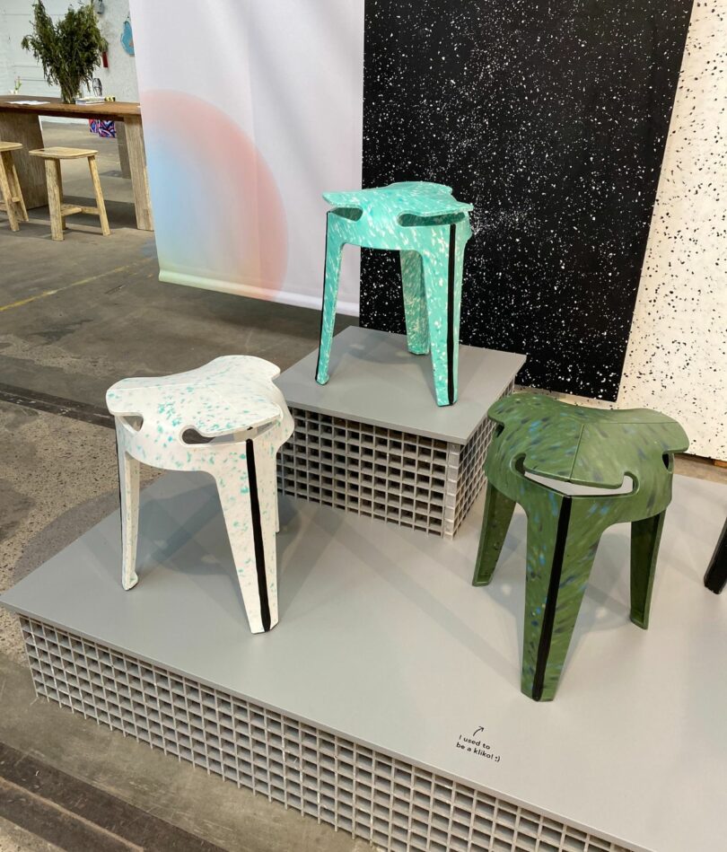 Three 3-legged stools each made from a single-sheet of flecked plastic material – one is dark green, one is mint green and one is cream colored. 