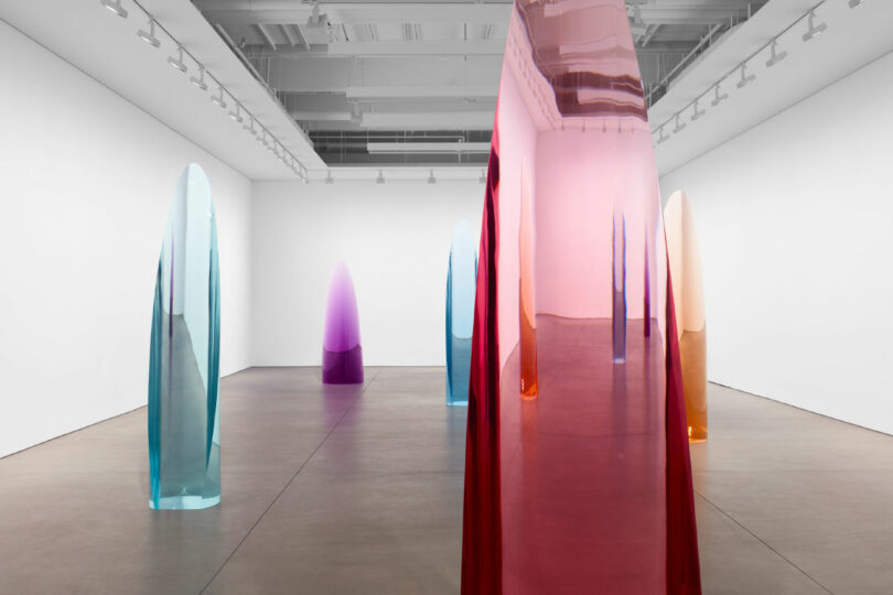 A open gallery space with cylindrical, transparent colored sculptures.