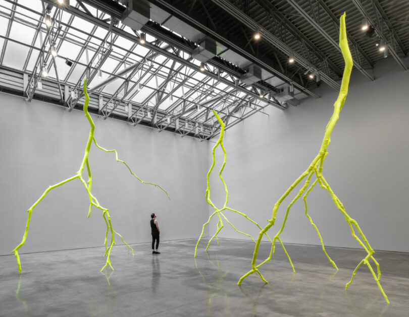 Visitor stands among 3 massive yellow sculptures
