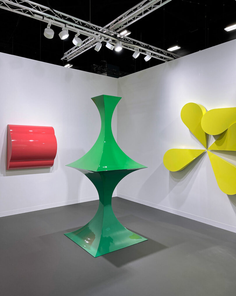three abstract sculptures in red, green, and yellow in a gallery space
