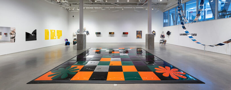Perspective of interactive dance floor made of orange, black, dark green, and silver metallic tiles in industrial gallery space.