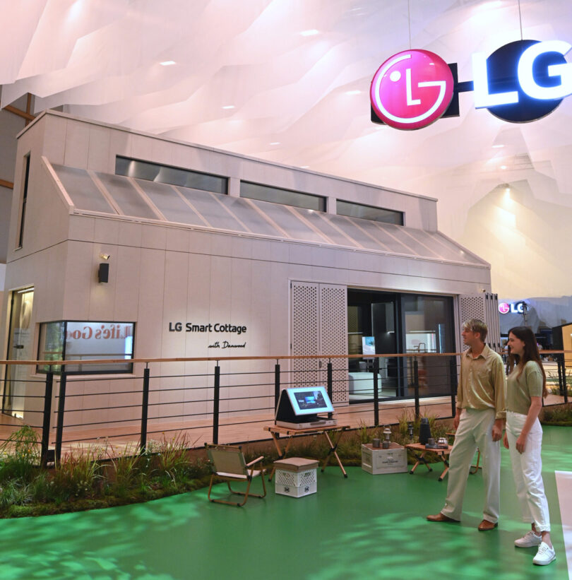 Exterior of LG Smart Cottage showcase home at IFA 2023 with man and woman looking at the home standing on faux grass.
