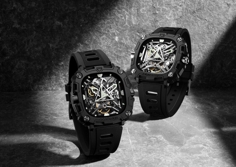 Two black and silver CIGA Design Eye of Horus mechanical wristwatches in a dramatically lit and shadowed stone backdrop.