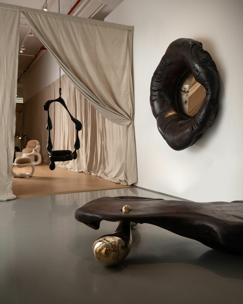 partial gallery view of bulbous dark wood mirror on wall and sculptural chaise underneath